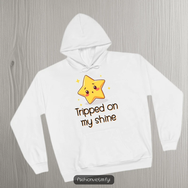 Funny hoodie with a cute star character tripping over its own sparkle with a surprised expression, offering comfort and a chuckle.